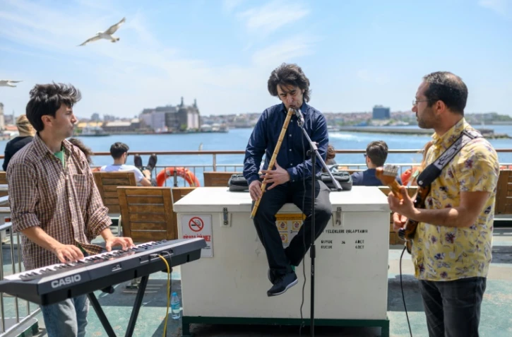 Le musicien Oguzhan Erdem (au centre) joue du ney, avec un guitariste et un pianiste, sur un ferry traversant le Bosphore Ă Istanbul le 16 mai 2019