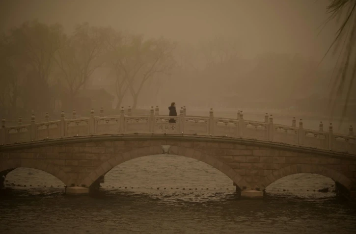 Une femme traverse un pont pendant une tempête de sable à Pékin le 15 mars 2021