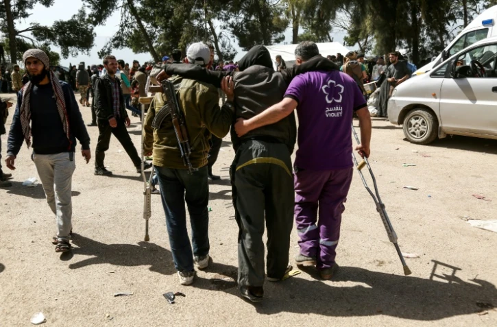 Un rebelle syrien armé d'une Kalachnikov et un membre d'une ONG locale portent un blessé à leur arrivée à Qalaat al-Madiq, dans la province syrienne de Hama, après leur évacuation de la Ghouta orientale, le 27 mars 2018