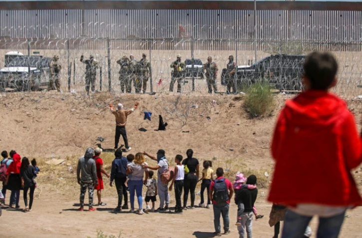 Des migrants cherchant à entrer aux Etats-Unis devant une barrière de fil barbelé et des agents de la Garde nationale du Texas, à la frontière entre le Mexique et les Etats-Unis, à Ciudad Juarez, le 13 mai 2024