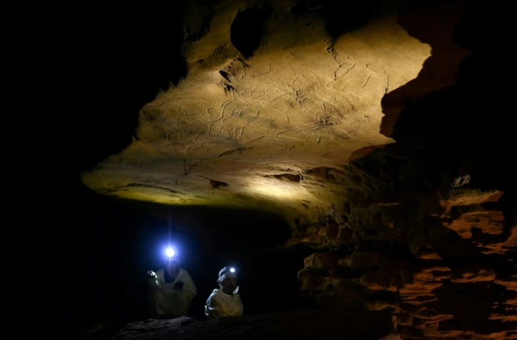 Des scientifiques éclairent avec leurs torches des gravures sur roche datant d'environ 30 000 ans lors d'une visite exclusive accordée par la DRAC de Nouvelle-Aquitaine, à l'intérieur de la grotte de Cussac, le 20 février 2025 au Buisson-de-Cadouin, en Dordogne