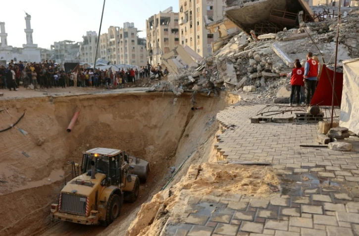 Des habitants et des membres de la Croix rouge regardent un tractopelle creuser, selon les autorités locales pour chercher les corps des otages, le 17 octobre 2025 à Khan Yunes
