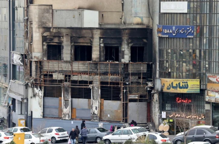 Des passants le 19 janvier 2026 devant un immeuble détruit lors des manifestations à Téhéran, en Iran