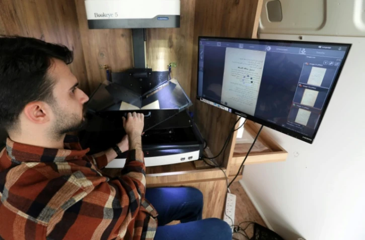 Un membre du Centre des arts et de la culture du Kurdistan (KCAC)scanne les pages d'un livre ancien pour en faire une copie numérique, le 13 février 2024 à Dohouk, dans la région du Kurdistan autonome, dans le nord de l'Irak