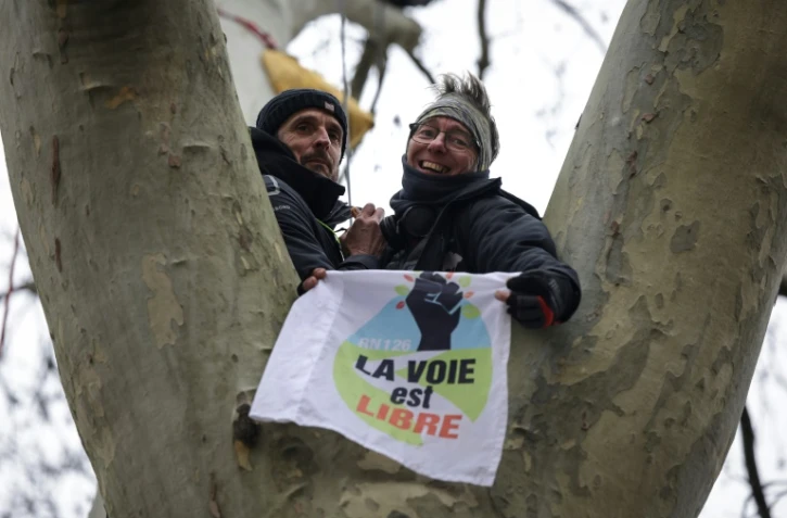Thomas Brail (g.), militant écologiste et fondateur du GNSA (Groupe national de surveillance des arbres), et Tanus, membre du GNSA, tiennent un drapeau portant l'inscription "La voie est libre" devant le tribunal administratif de Toulouse, le 17 février 2025