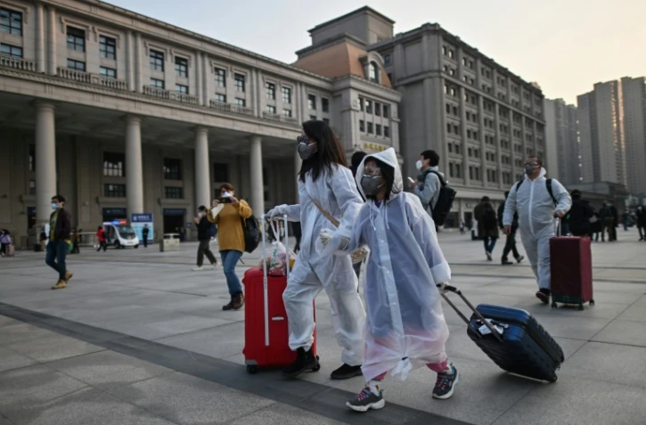 Des passagers portant des masques et des combinaisons pour se protéger se rendent à la gare de Wuhan, dans le centre de la Chine, le 8 avril 2020, après la levée des restrictions pour quitter la ville, berceau de la pandémie de coronavirus.


