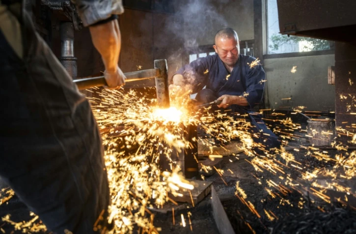 Le forgeron Akihira Kawasaki (d) maintient l'acier sur une enclume tandis que son apprenti Toru Watanabe martèle le métal pour forger des lames de katana, le 9 janvier 2026 à Misato, au Japon