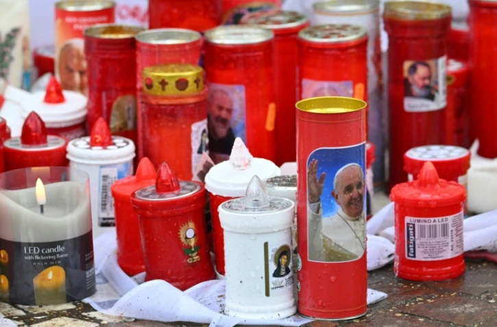 Des bougies déposées au pied de la statue de Jean-Paul II devant l'hôpital Gemelli à Rome où le pape François est soigné pour une pneumonie, le 14 mars 2025