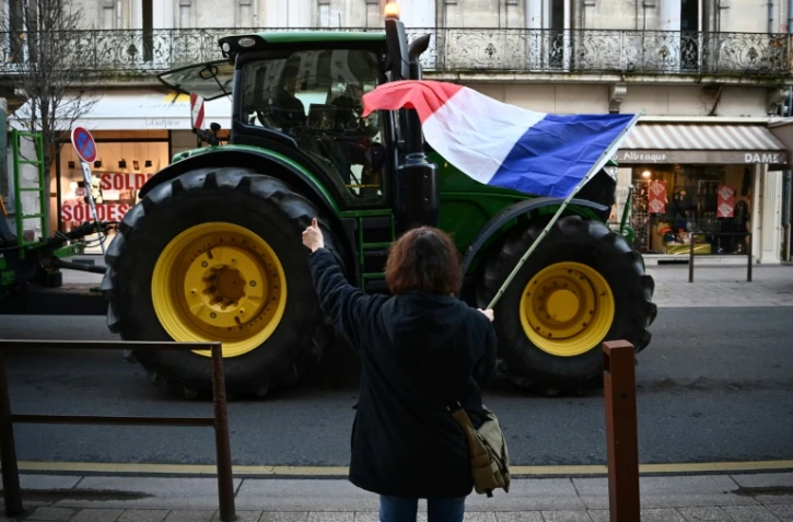 Un agriculteur manifeste avec son tracteur, salué par une passante avec un drapeau français, à Agen, dans le Lot-et-Garonne, le 25 janvier 2024