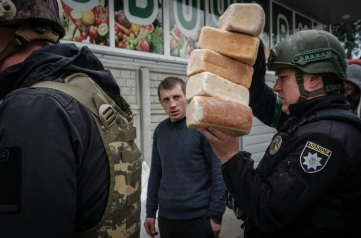 Des officiers de police ukrainiens livrent du pain, le 2 mai 2022, aux résidents restés dans la ville de Lyman à l'est de l'Ukraine malgré l'offensive des troupes russes