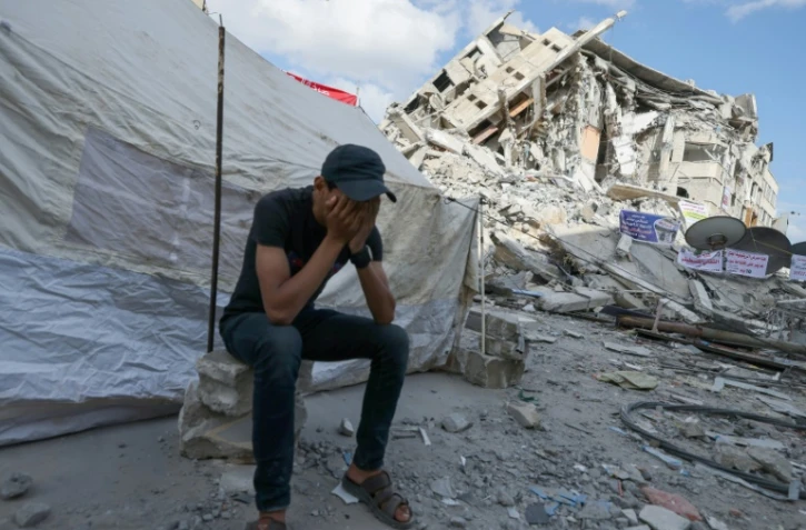 Un Palestinien couvre son visage avec les mains, assis devant une tente installée au milieu des décombres dans la bande de Gaza, le 23 mai 2021