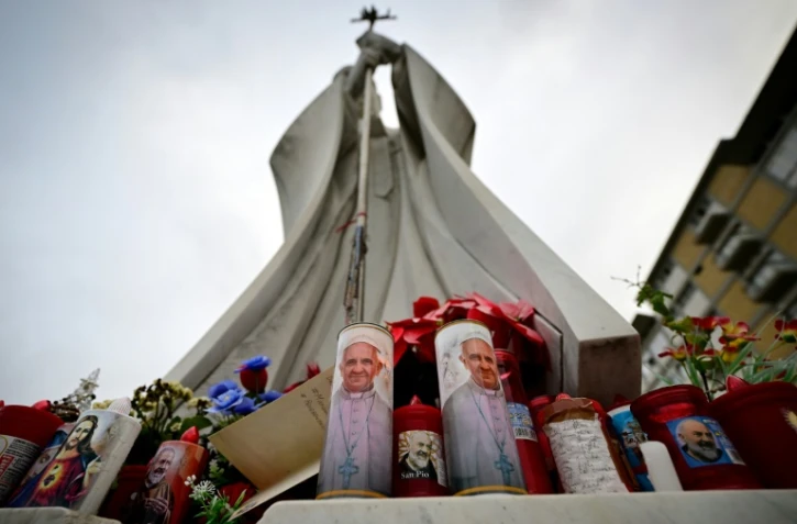 Des bougies à l'effigie du pape François et de Padre Pio déposées au pied de la statue de Jean Paul II devant l'hôpital Gemelli où le pape François est hospitalisé, le 19 février 2025 à Rome