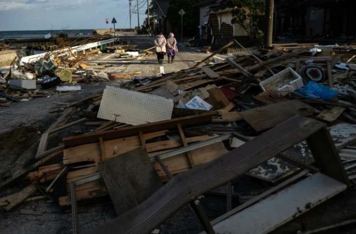 Des personnes marchent sur une route jonchée de débris le 5 janvier 2024 à Shiromaru au Japon après un tsunami provoqué par le séisme du Nouvel An