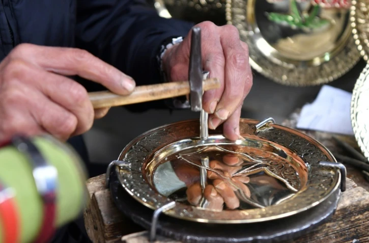 Un artisan grave un dessin sur une plaque de cuivre dans sa boutique des souks de la médina de Tunis, le 7 décembre 2023