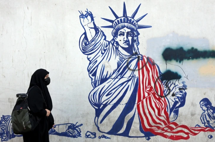 Cette photo, prise le 26 février 2026, montre une Iranienne voilée passant devant une fresque anti-américaine située à côté de l'ancienne ambassade des États-Unis à Téhéran.