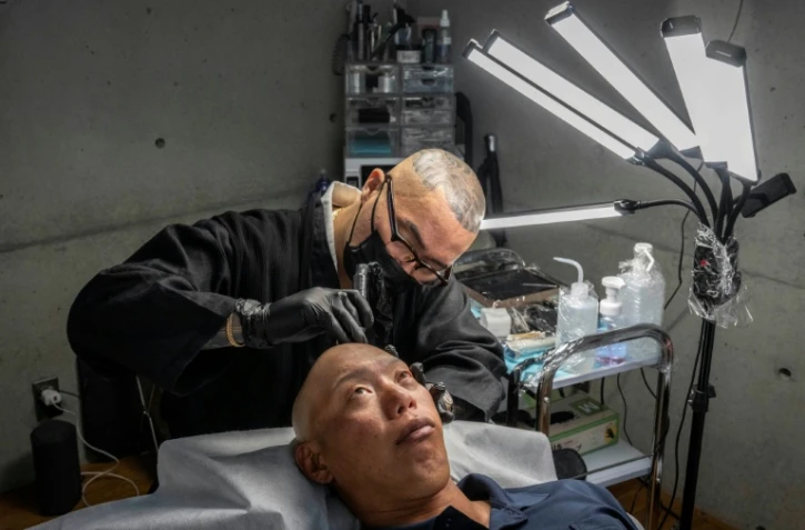 Remy, tatoueur professionnel, réalise une intervention de micropigmentation du cuir chevelu sur un client, dans son studio de Ginowan, à Okinawa au Japon, le 19 mai 2026