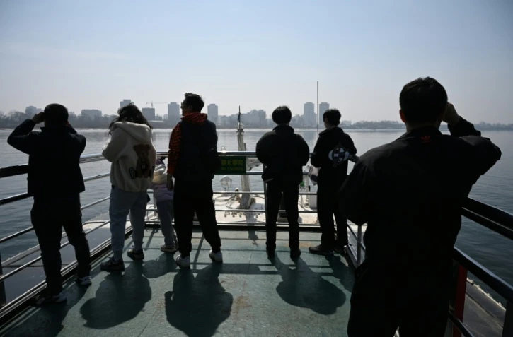 Des touristes observent la ville nord-coréenne de Sinuiju (arrière-plan) depuis un bateau touristique sur le fleuve Yalu, dans la ville frontalière de Dandong, dans le nord-est de la Chine, le 26 mars 2026