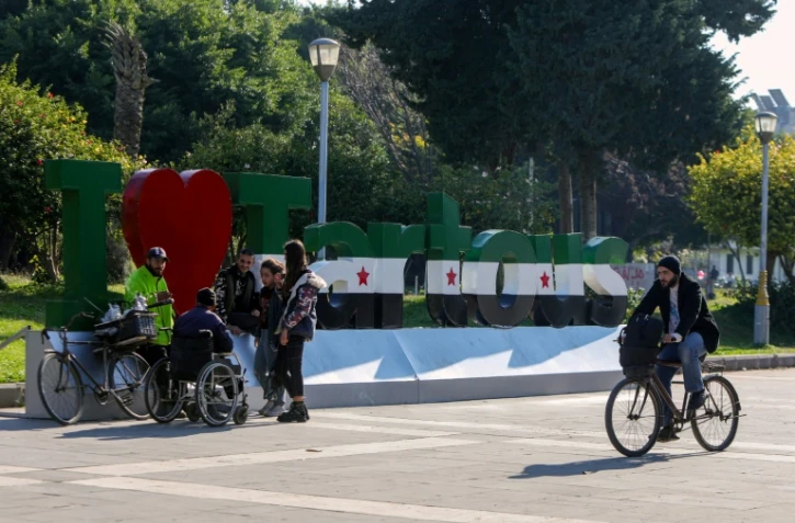 Des Syriens à Tartous, dans l'ouest de la Syrie, devant une enseigne peinte aux nouvelles couleurs du pays, le 17 décembre 2024