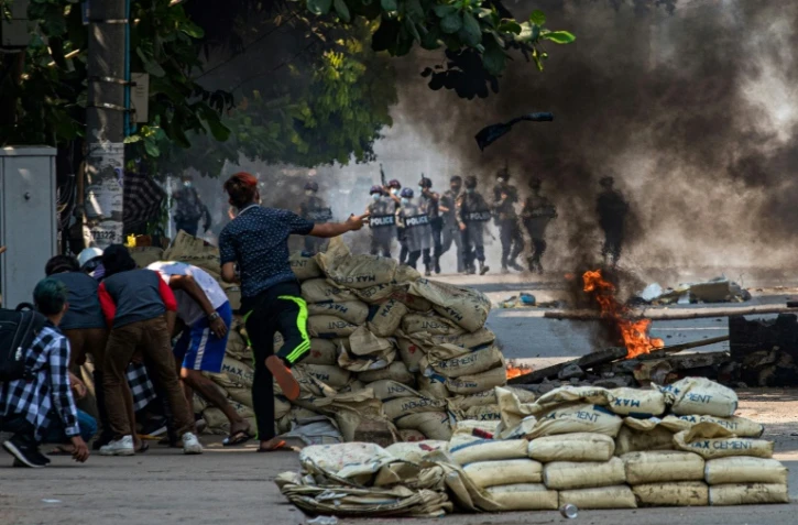 Un manifestant jette un projectile en direction des forces de l'ordre alors que d'autres se protègent derrière une barricade, protestant contre le coup d'Etat militaire, le 17 mars 2021 à Rangoun