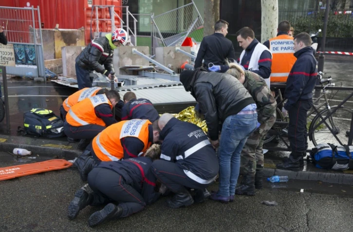 Les pompiers administrent les premiers soins à un couple à Paris, blessé par la chute d'un panneau publicitaire en raisons de fortes rafales de vent, le 8 février 2016