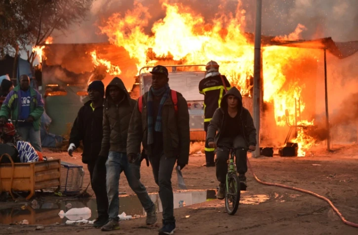 De jeunes migrants quittent la "Jungle" de Calais où un pompier tente d'éteindre un feu, le 26 octobre 2016