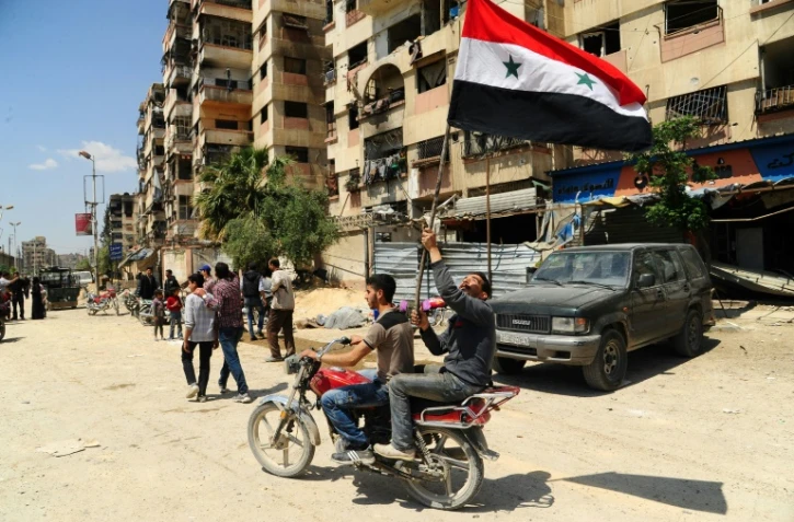 Photo fournie par l'agence de presse syrienne officielle Sana montrant un homme à moto tenant le drapeau syrien dans une rue de Douma, le 14 avril 2018