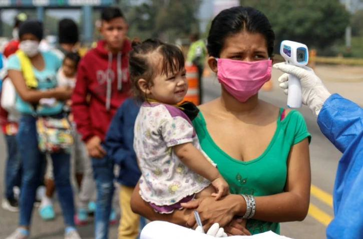 Des employés du ministère de la Santé prennent la température de Vénézuéliens retournant au pays depuis la Colombie, le 4 avril 2020 sur le pont international Simon Bolivar, à Cucuta