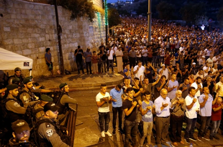 Des forces de sécurité israéliennes regardent des Palestiniens prier à l'extérieur de l'esplanade des Mosquées à Jérusalem, le 24 juillet 2017