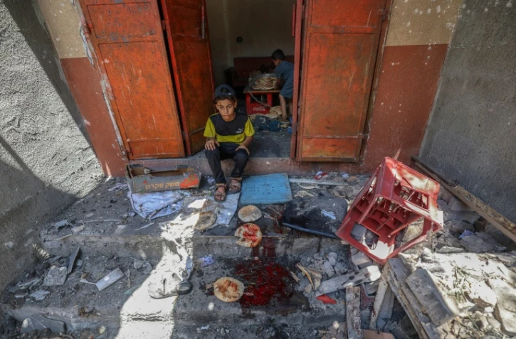 Des enfants palestiniens récupèrent du pain dans une boulangerie détruite par des frappes israéliennes dans le camp de réfugiés de Nousseirat, dans le centre de la bande de Gaza, le 8 mai 2025