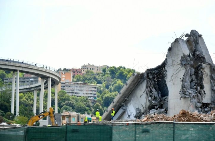 Des ouvriers sur le site et aux côtés de débris du pont Morandi de Gênes, le 13 août 2019, la veille du premier anniversaire de son effondrement