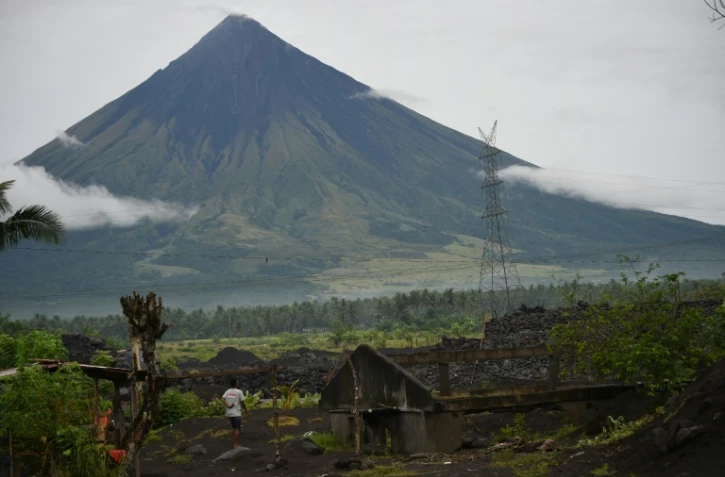 Un habitant à côté d'une maison à moitié ensevelie par le sable et les roches apportés par le volcan Mayon, en arrière-plan, après les fortes pluies du typhon Goni en 2020 dans le village de San Francisco à Guinobatan aux Philippines, le 5 octobre 2021