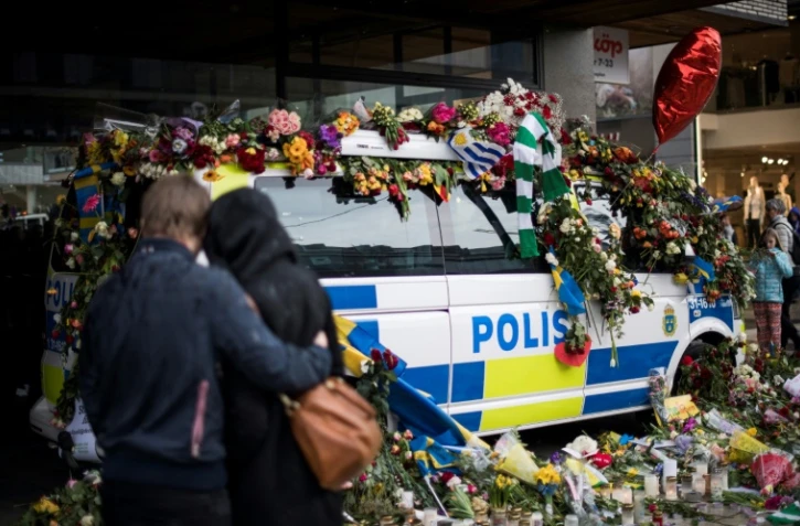 Des personnes se recueillent devant un véhicule de police recouvert de fleurs sur le site d'un attentat au camion-bélier, le 10 avril 2018 à Stockholm