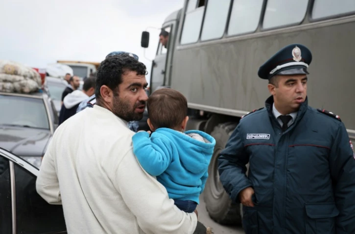 Un réfugié portant un enfant s'entretient avec un policier près de la ville frontalière de Kornidzor, en Arménie, le 25 septembre 2023