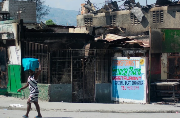Une femme passe devant un un rstaurant brûlé par des bandes armées, le 12 mars 2024 à Port-au-Prince, en Haïti