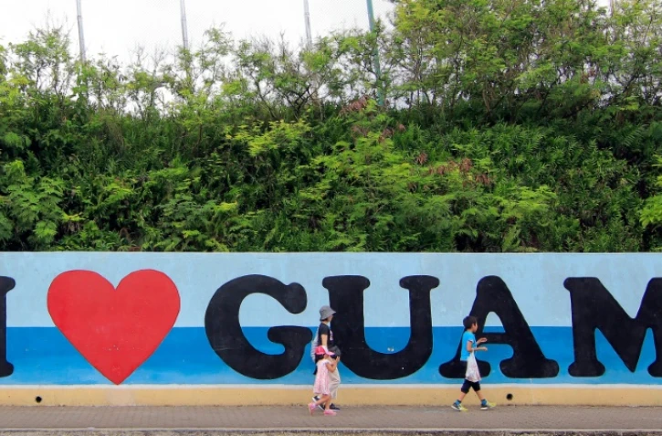 Des touristes passent devant une affiche "I love Guam", sur l'île de Guam dans l'océan pacifique, le 11 août 2017 