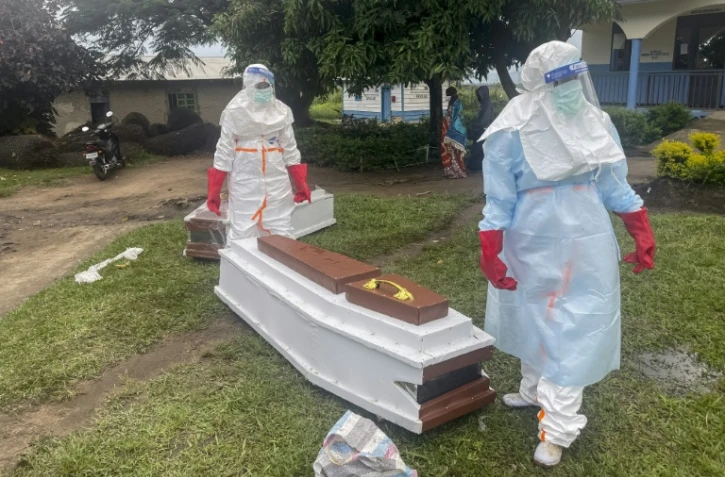 Des membres du personnel médical, en combinaisons de protection, près du cercueil d'un patient décédé du virus Ebola dans un hôpital à Rwampara, le 21 mai 2026 en RDC