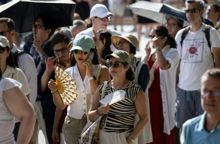 Des touristes avec des éventails devant la cathédrale Notre-Dame, le 16 août 2025 à Paris
