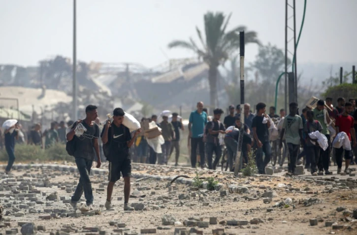 Des déplacés palestiniens portent des produits alimentaires obtenus à un point de distribution du centre de la bande de Gaza, le 26 juillet 2025