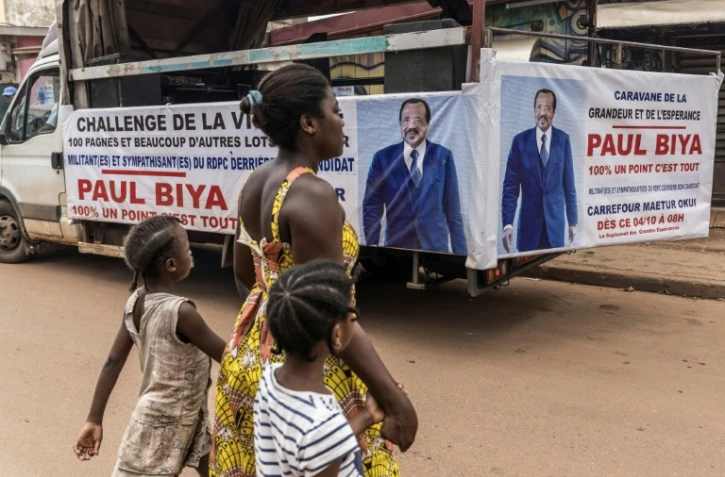 Une femme et ses enfants traversent la rue près d'un camion de campagne du président sortant du Cameroun, Paul Biya, à Yaoundé le 11 octobre 2025