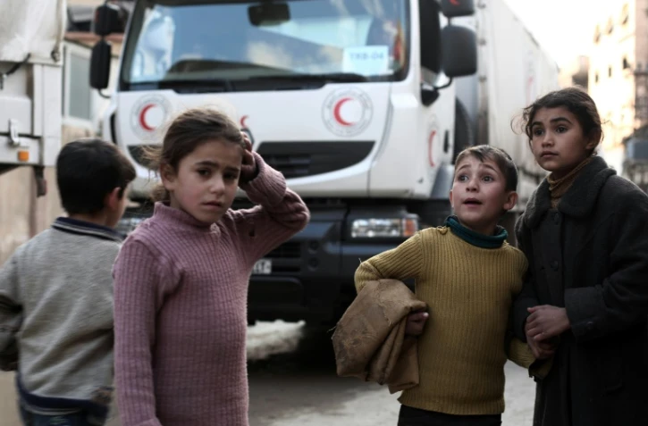 Des enfants syriens devant un convoi d'aide humanitaire du croissant rouge à Kafr Batna, dans les environs de Damas, le 23 février 2016
