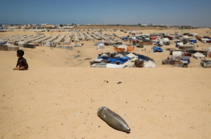 Un obus non explosé non loin d'un enfant assis sur le sable près d'un camp de fortune pour Palestiniens déplacés dans la zone de Tel al-Sultan à Rafah, dans le sud de la bande de Gaza, le 30 mai 2024