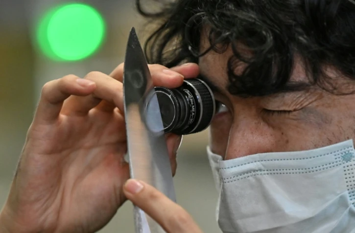 Un employé du fabricant japonais de couteaux Sumikama inspecte une lame à l'aide d'une loupe dans son usine de Seki, au Japon, le 22 juillet 2025
