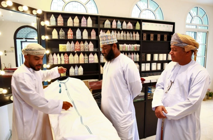 Un vendeur de dishdashas, robe traditionnelle portée par les hommes à Oman, montre un modèle à des clients, le 10 janvier 2022 à Mascate