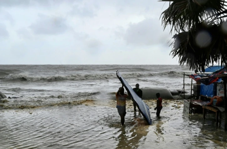 Des hommes transportent leur atelier de fortune au bord de la mer à titre préventif lors des pluies à Kuakata le 26 mai 2024, avant l'arrivée dimanche soir du cyclone Remal au Bangladesh.