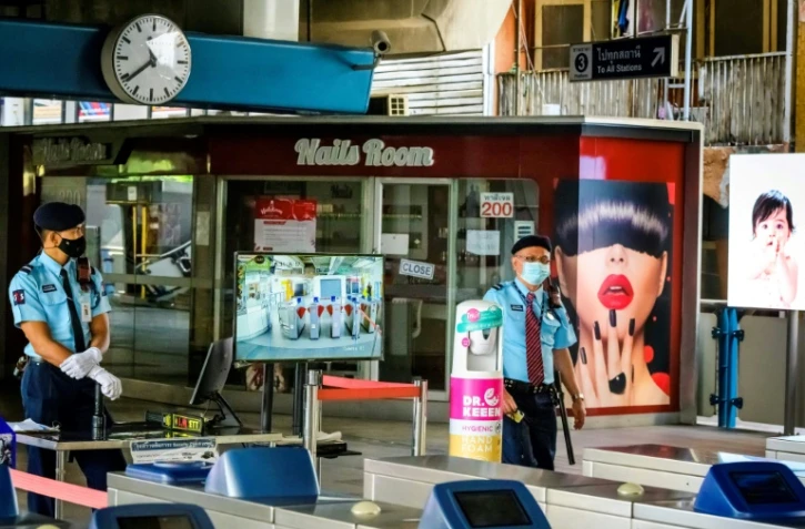 En Thaïlande, des forces de sécurité postées à un point de contrôle des températures, près d'un salon de manucure fermé, à une station du métro de Bankgok le 2 janvier 2021