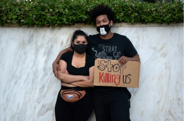 Un couple pose avec un écriteau qui demande "Arrêter de nous tuer", à Los Angeles le 27 mai 2020, après la mport de George Floyd, un Afroaméricain asphixié par la police lors d'une interpellation