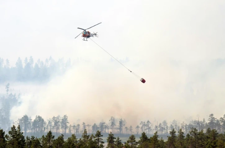 Un hélicoptère bombardier d'eau survole un massif forestier en feu à Korskrogen, en Suède, le 25 juillet 2018.