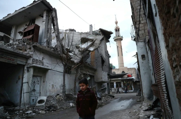 Un enfant marche dans une rue bordée de maisons détruites, le 9 janvier 2017 à Douma, près de Damas, en Syrie