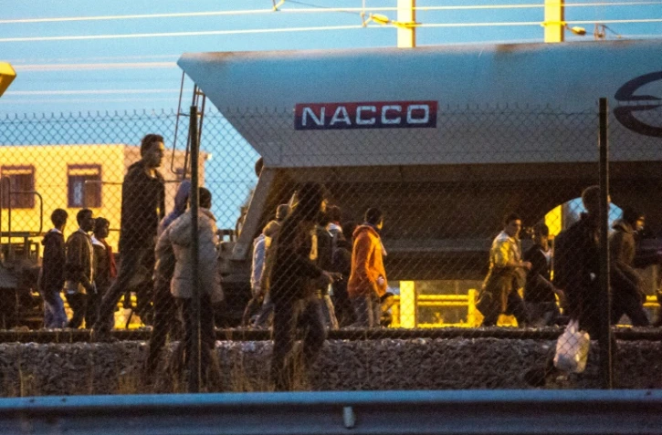 Des migrants marchent sur la voie ferrée en direction du terminal d'Eurotunnel le 11 août 2015 à Fréhun