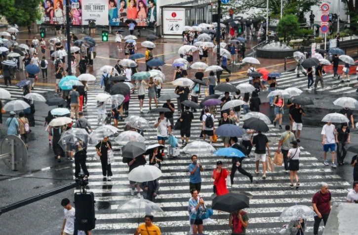 Des piétons s'abritent de la pluie, à l'approche du typhon "Ampil", le 16 août 2024 à Tokyo